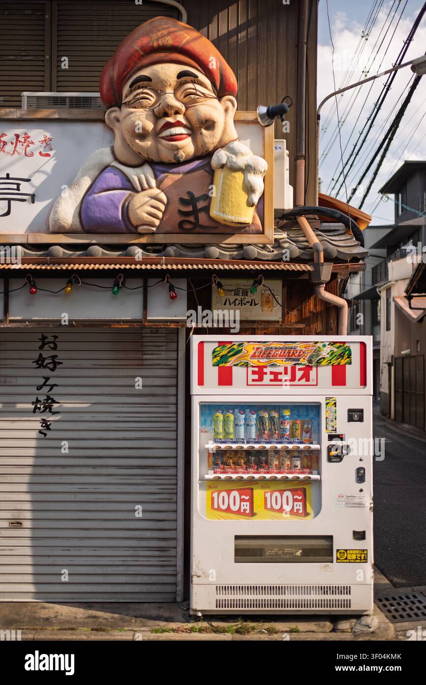 Un distributeur automatique de boissons moderne et coloré debout à côté d'une statue fantaisiste de personnage de dessin animé dans une rue, Kyoto, Japon Banque D'Images