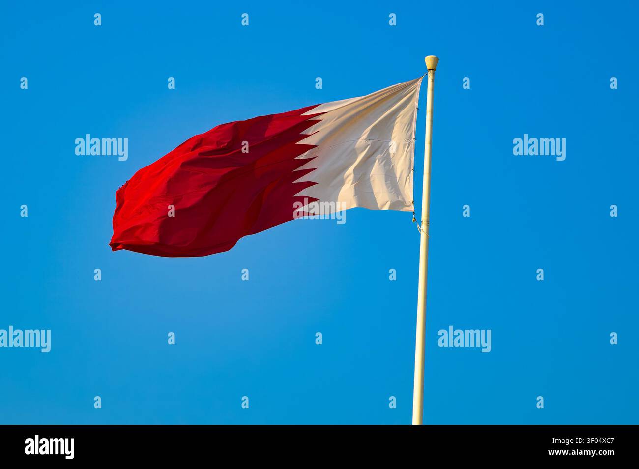 Drapeau national du Qatar agitant sur le mât de drapeau contre le ciel bleu clair Banque D'Images
