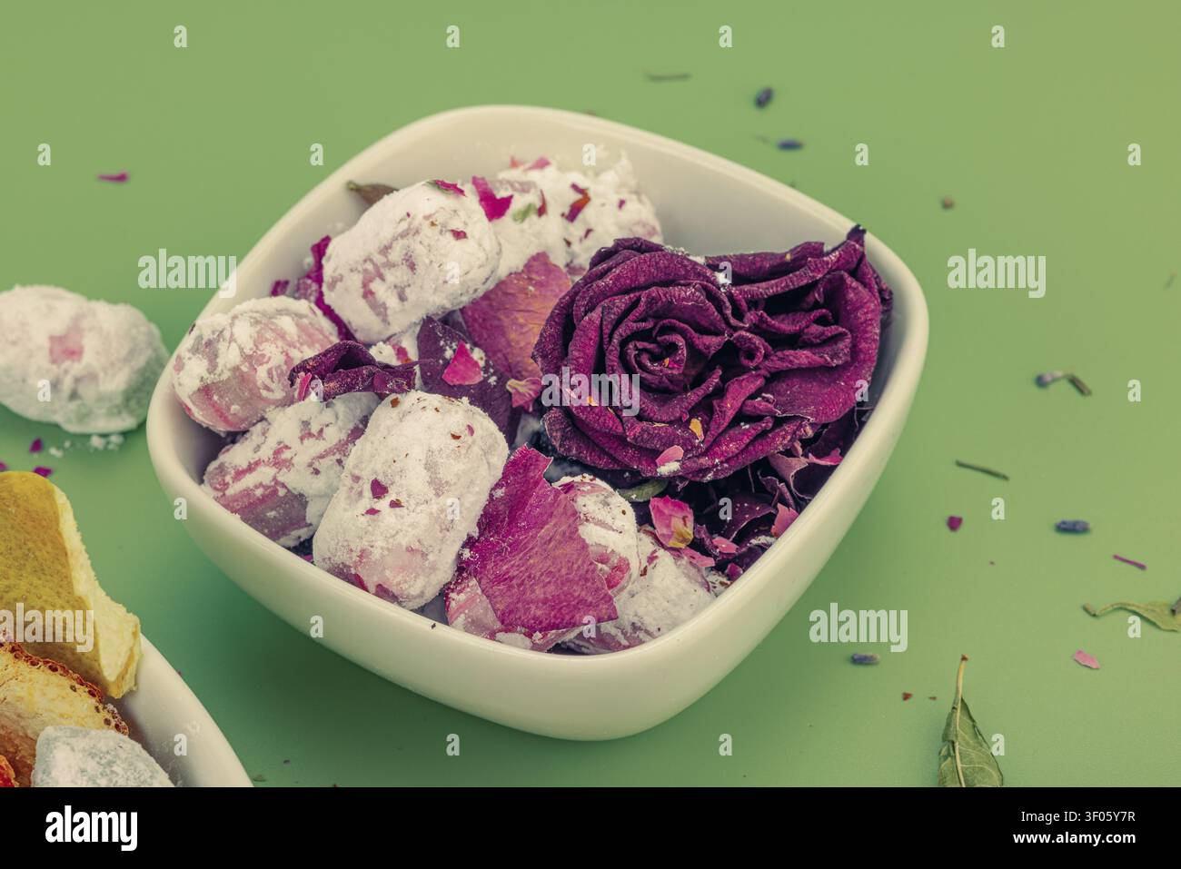 Bonbons de fleurs faits maison dans du sucre en poudre avec des roses séchées, de la lavande et des spirales de zeste d'orange dans des bols sur fond vert. Des sucreries botaniques naturelles a Banque D'Images