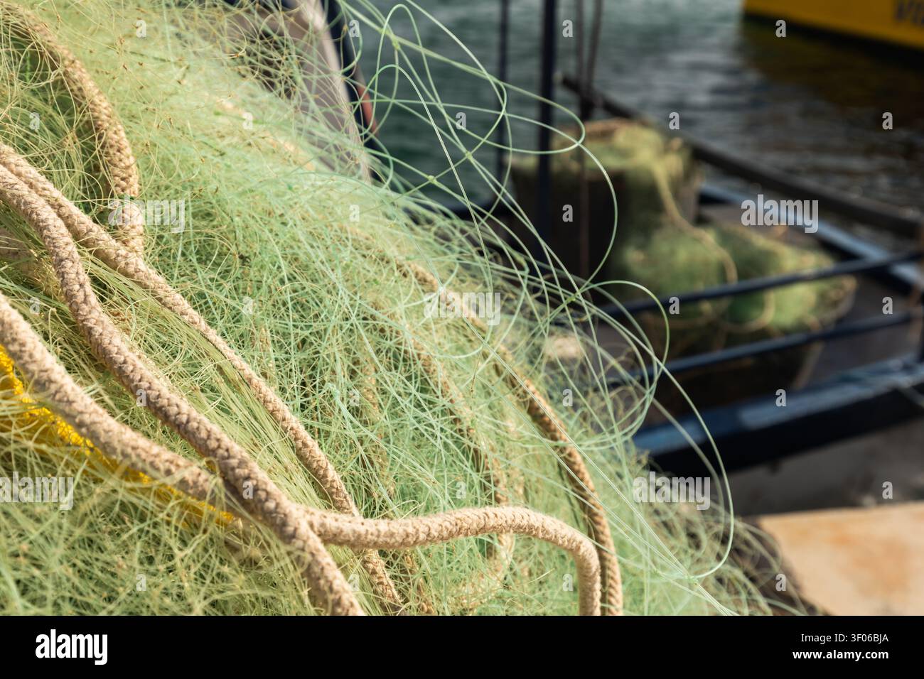 Gros plan détaillé d'un filet de pêche enchevêtré et d'une corde épaisse sur un pont de bateau de travail au port, montrant la texture, les lignes et les engins maritimes dans une lumière douce. Banque D'Images