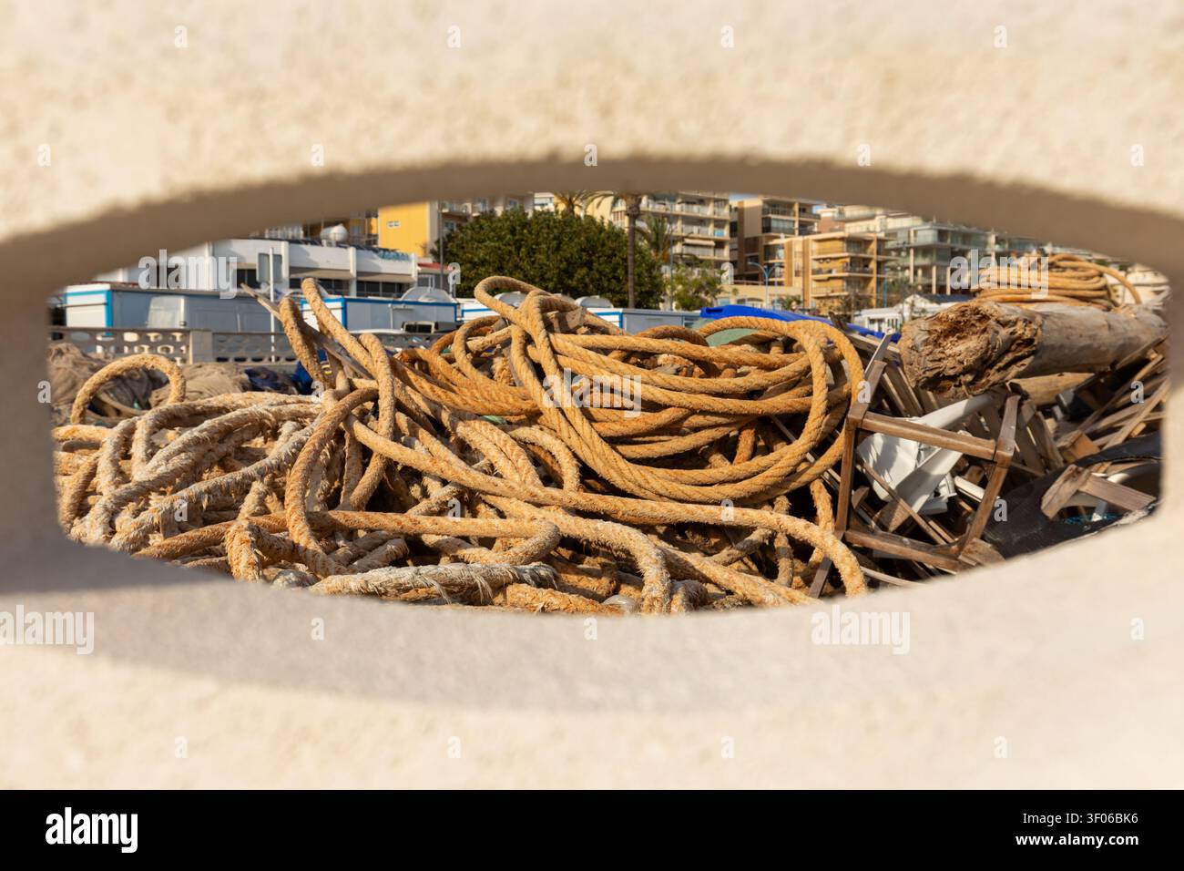 Cordes maritimes altérées et débris de bois empilés sur la plage de Calpe, vus à travers un cadre naturel, avec des appartements côtiers en arrière-plan sur un ensoleillé Banque D'Images