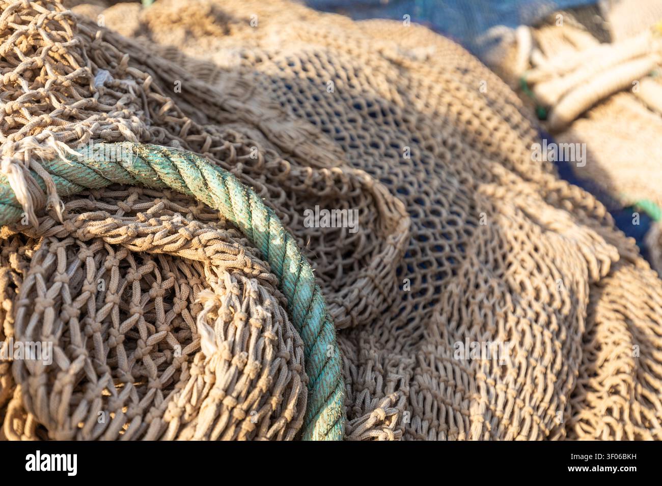 Gros plan détaillé des filets de pêche enchevêtrés avec corde enroulée, montrant la texture tissée rugueuse et l'usure marine en plein soleil chaud, idéal pour nautique, côtier, Banque D'Images