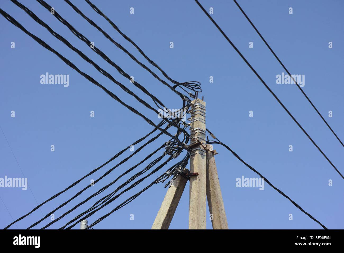 Prise de vue à faible angle d'un poteau utilitaire en béton avec un enchevêtrement complexe de lignes électriques noires sur un fond de ciel bleu clair. Banque D'Images