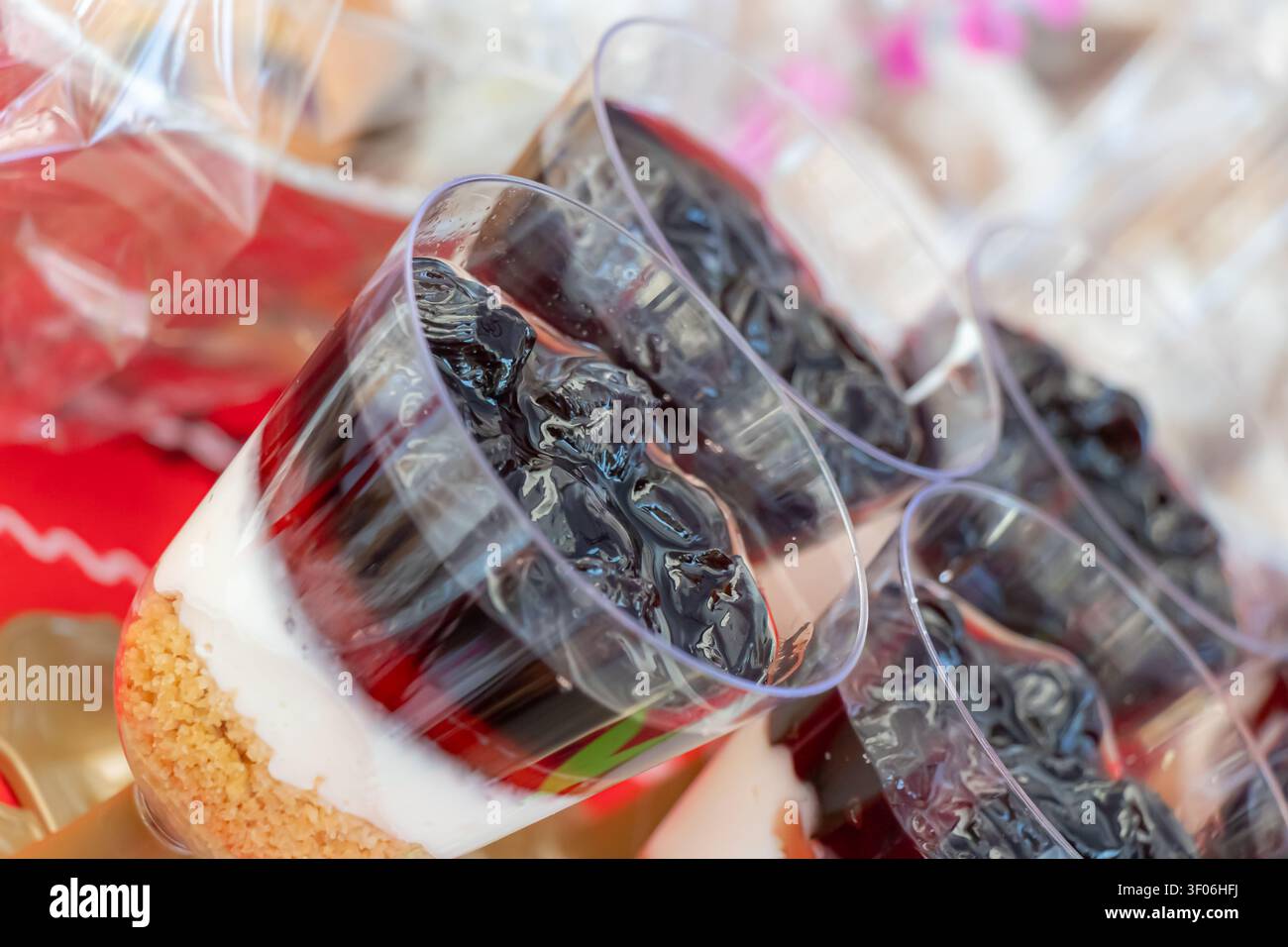 Close-up de coupes de dessert aux cerises en couches avec base de biscuit, crème et garniture de baies noires, disposées sur un présentoir de catering festif avec mise au point douce et co Banque D'Images