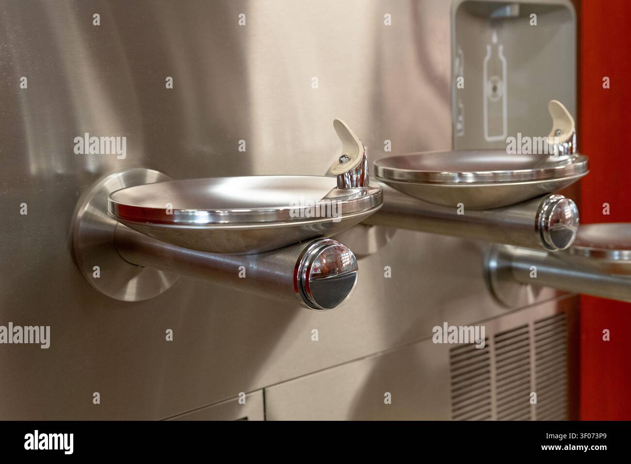 Un plan rapproché détaillé d'une fontaine à eau moderne à plusieurs niveaux en acier inoxydable avec une station de remplissage de bouteilles intégrée, montée contre warm-to Banque D'Images