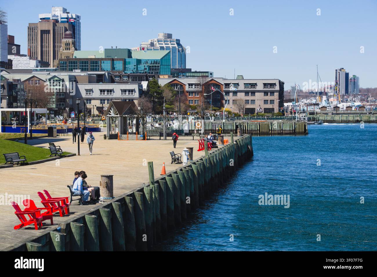 Des gens se détendent sur la promenade ensoleillée du front de mer de Halifax avec vue sur le port bleu et les bâtiments de la ligne d'horizon urbaine. Banque D'Images