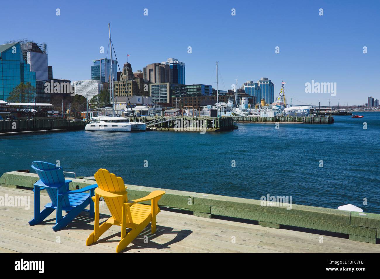 Chaises colorées sur le Boardwalk de Halifax avec vue sur le port et la skyline urbaine de la Nouvelle-Écosse, au Canada, par une journée ensoleillée. Banque D'Images