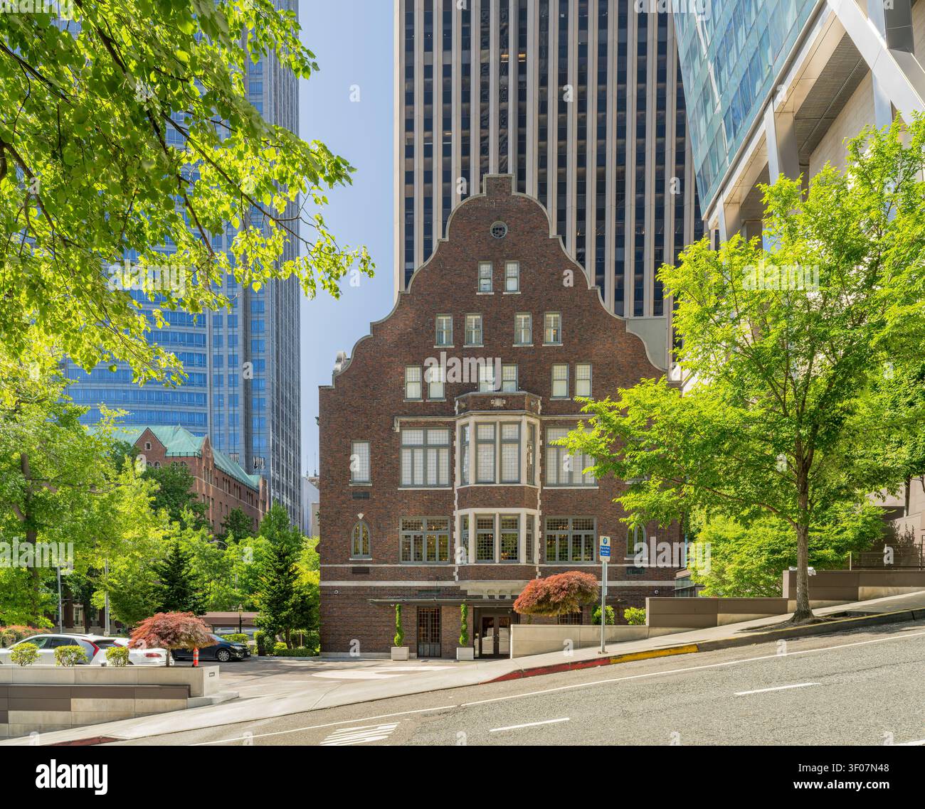 Un bâtiment en briques rouges avec une façade à pignon en escalier se dresse sur une rue de la ville entourée de gratte-ciel modernes et d'arbres verts. Banque D'Images