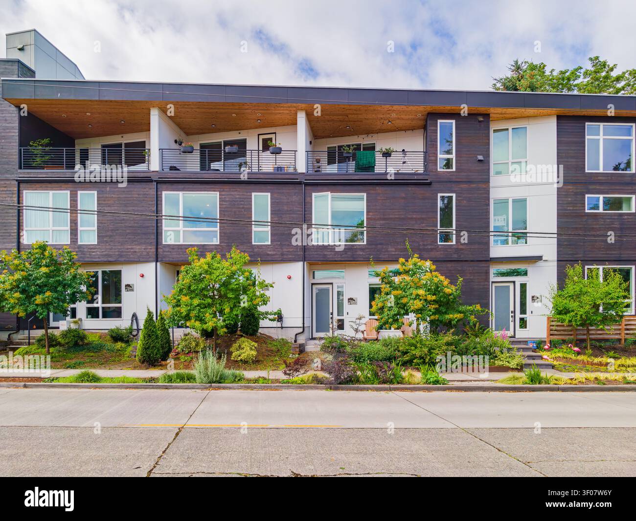 Complexe d'appartements contemporains décoré d'un parement en bois sombre, de touches blanches et de grandes fenêtres avec vue sur la rue et sur la cour avant aménagée. Banque D'Images