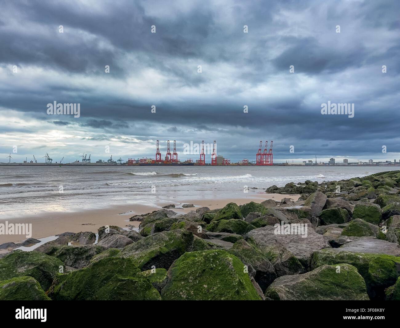 Plage de New Brighton avec des rochers couverts d'algues faisant face aux grues portuaires de Liverpool de l'autre côté de la rivière Mersey Banque D'Images