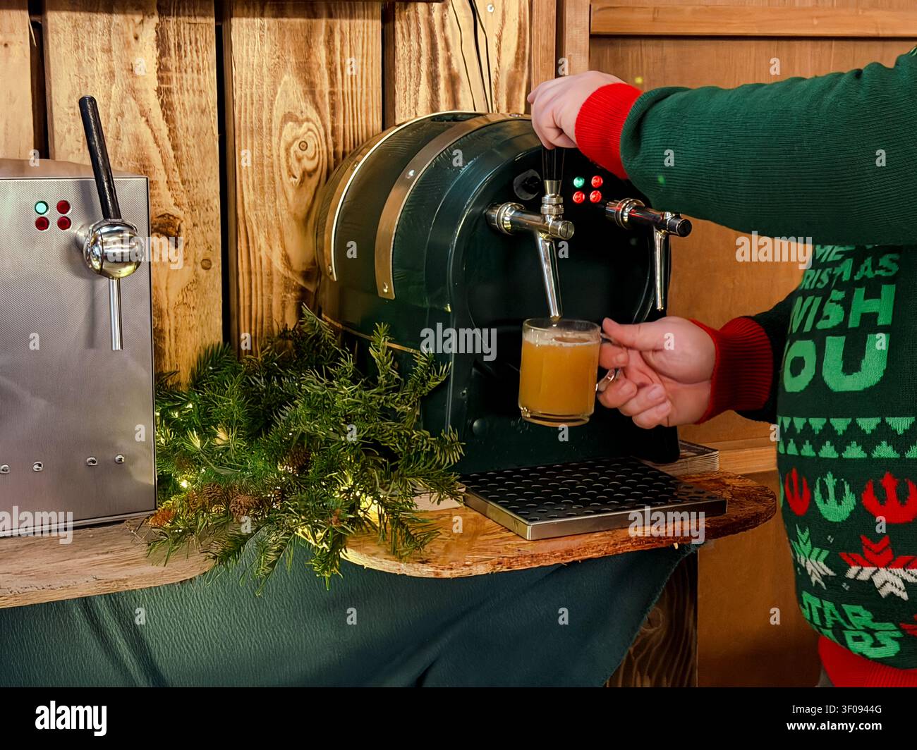 Personne en chandail festif versant du vin chaud d'un distributeur de boisson dans une tasse en verre Banque D'Images