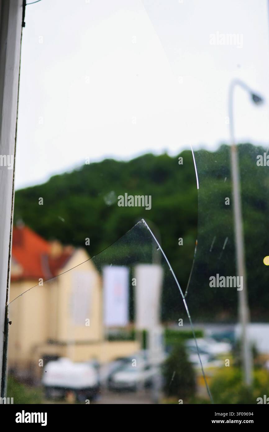 Close-up d'une fenêtre fissurée avec du verre brisé et un quartier résidentiel flou en arrière-plan, concept de dommage, de vandalisme ou de réparation. Banque D'Images