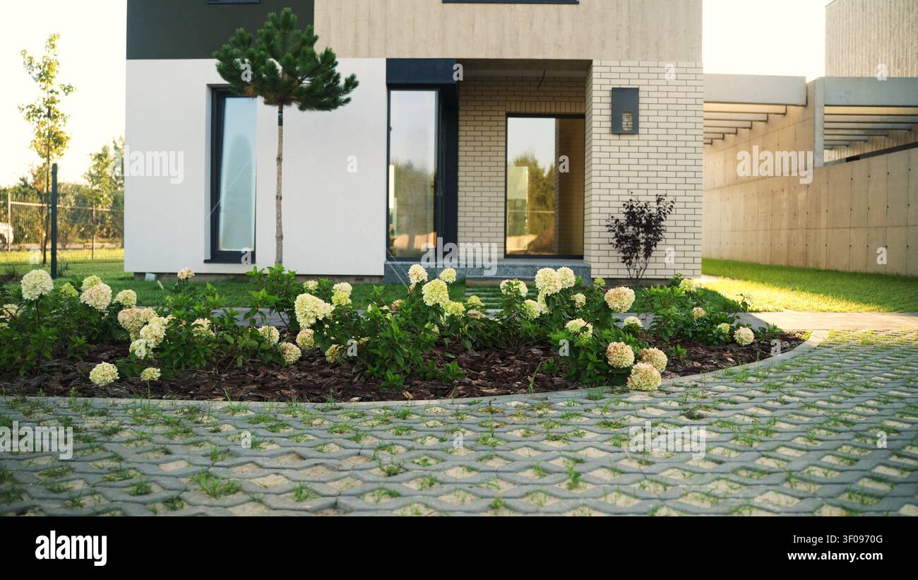 Façade de maison moderne avec jardin bien entretenu, présentant des hortensias en fleurs et un revêtement perméable dans la cour avant Banque D'Images