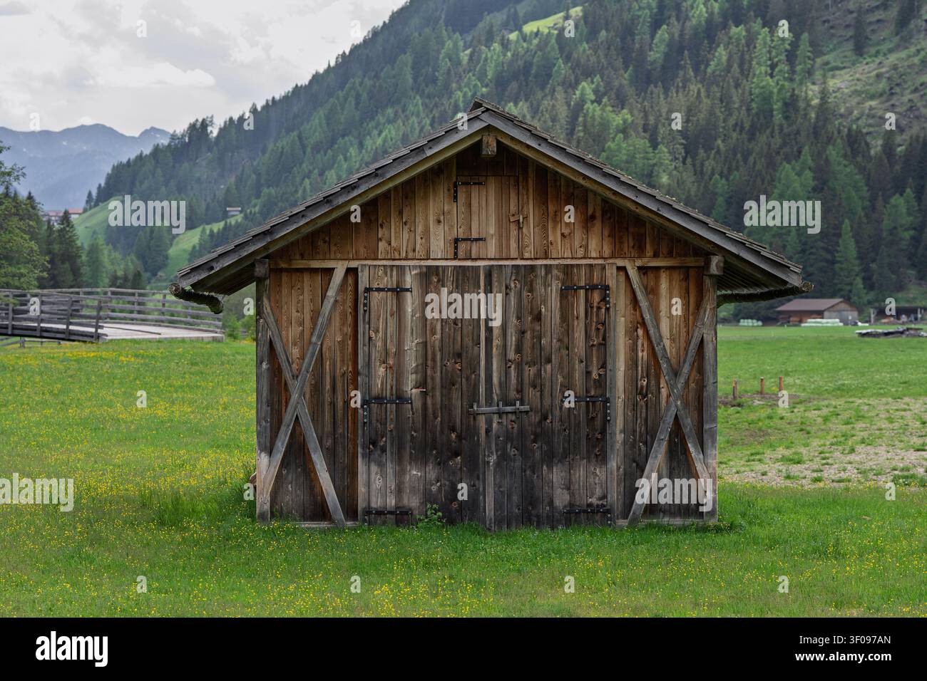 cabane en bois paisible dans un paysage rural avec des montagnes et un champ d'herbe en vue latérale, scène de campagne sereine aux tons verts et bruns, cadre naturel Banque D'Images