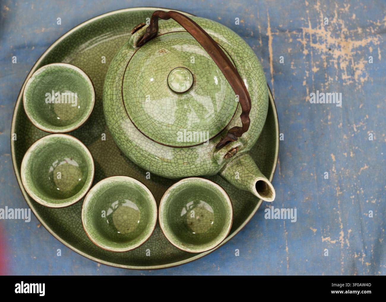 Vue de dessus d'un service à thé en céramique vintage vert émeraude avec vernis craquelé comprenant une théière et des tasses sur une surface bleue avec espace de copie. Banque D'Images