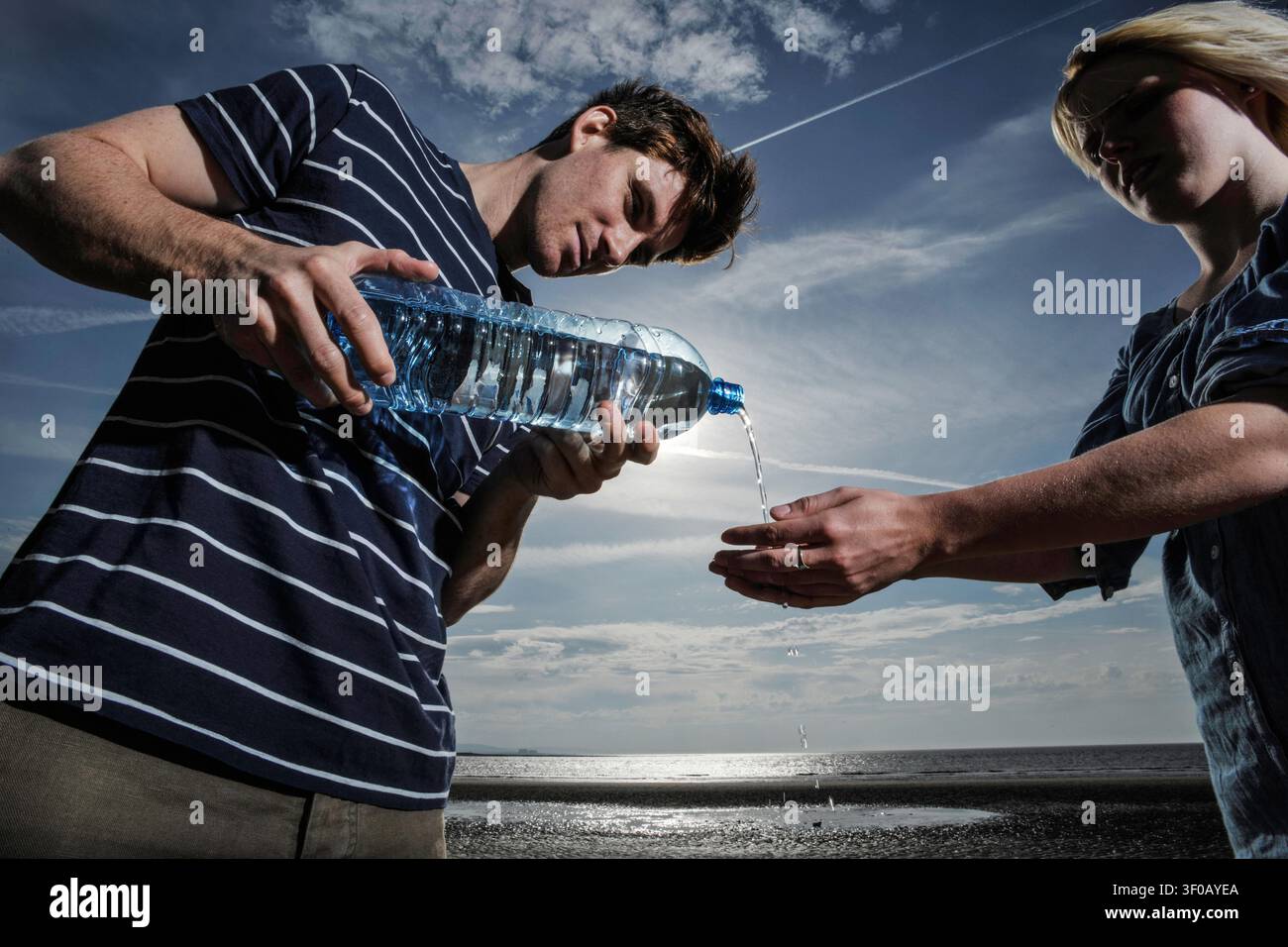 jeune homme lavant les mains d'une femme en versant de l'eau d'une bouteille en plastique sur une plage Banque D'Images