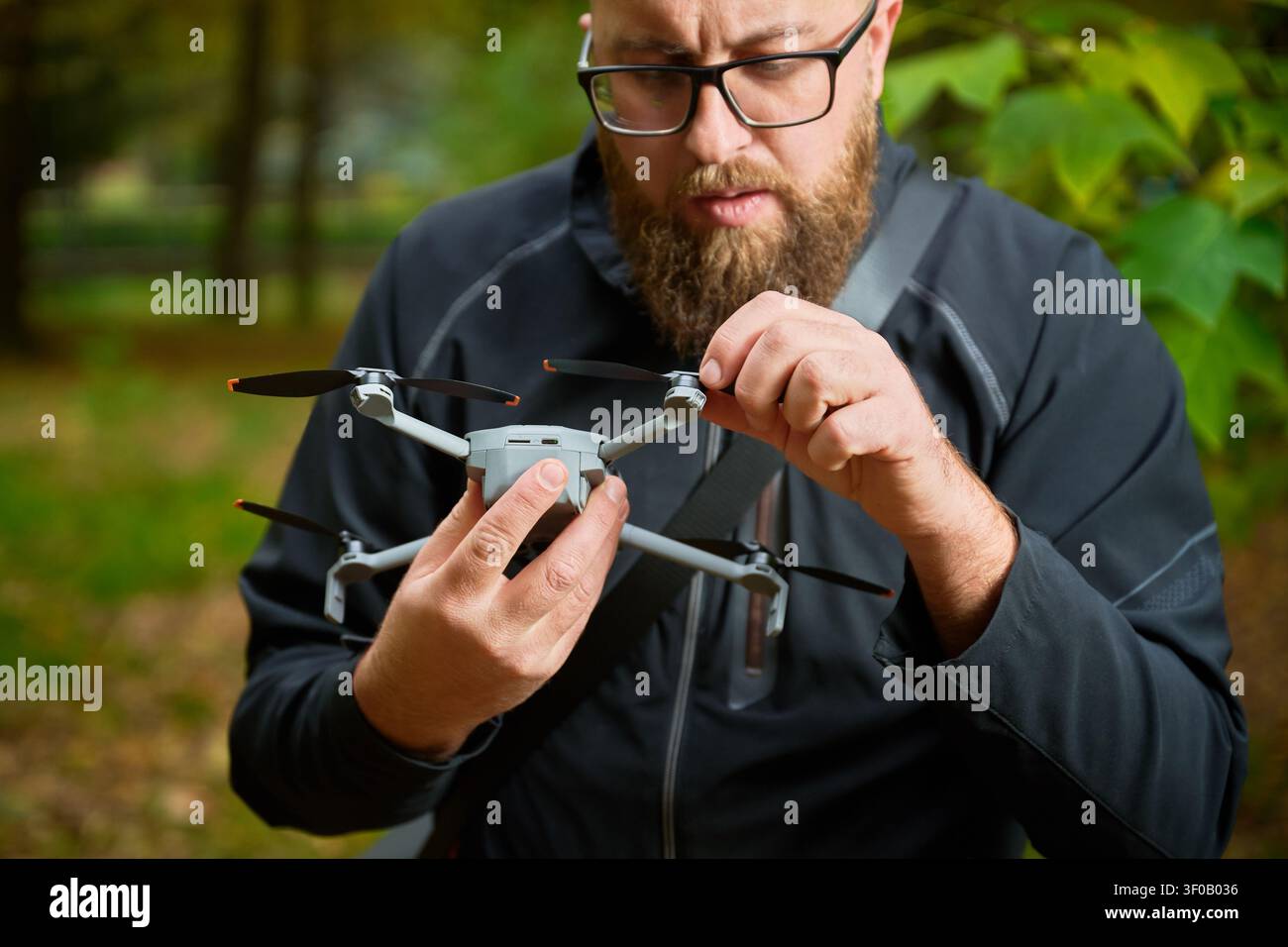 L'homme ajuste l'hélice du drone avant le vol. Homme barbu vérifiant les lames quadcopter dans le parc, assurant un état et une configuration appropriés, concept de technologie moderne et de maintenance Banque D'Images