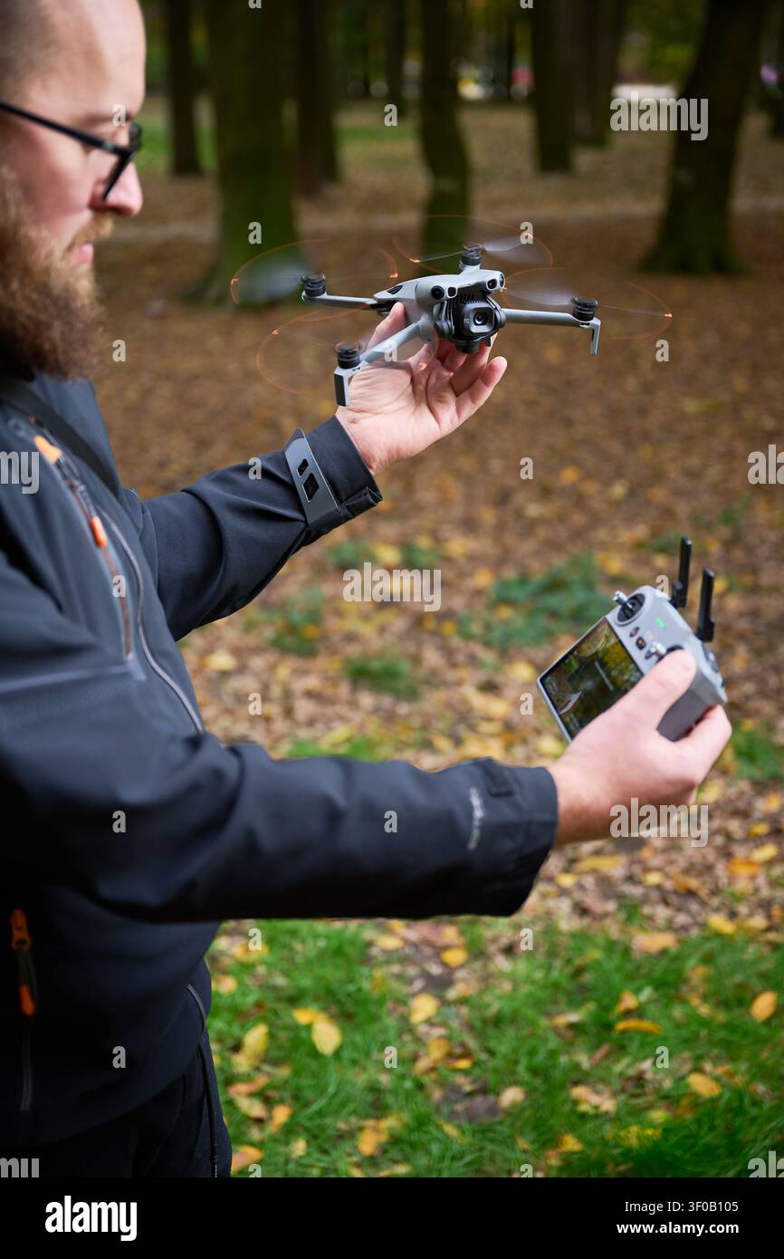 L'homme tient un drone volant et le surveille avec un contrôleur. Homme barbu opérant quadcopter dans un parc, contrôlant le vol pour la photographie aérienne, concept de technologie moderne et passe-temps Banque D'Images