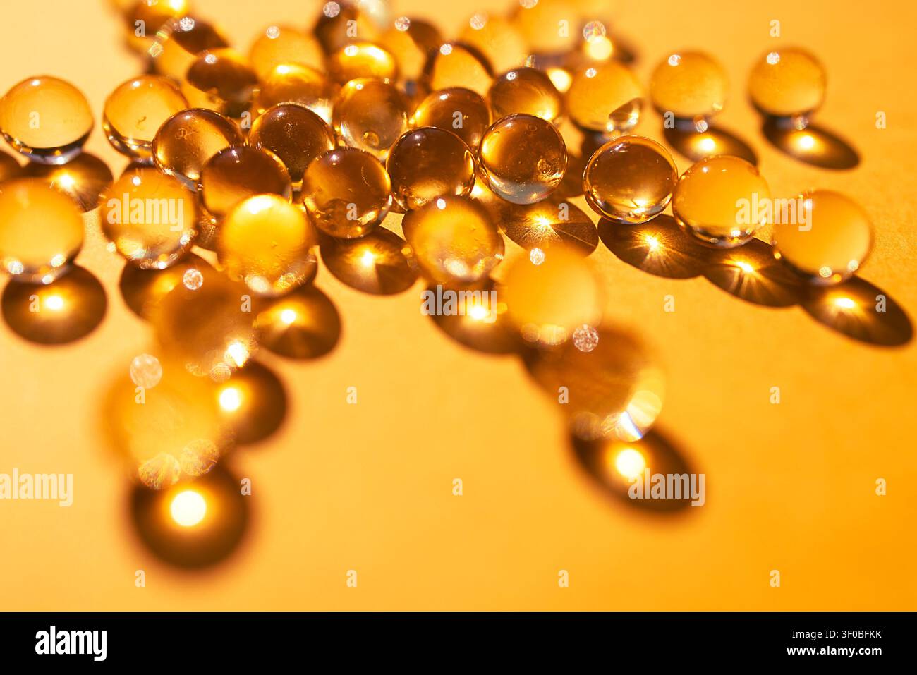 Des gouttes d'eau transparentes sont disposées sur une surface dorée, reflétant la lumière et projetant des ombres douces, créant une texture visuellement attrayante Banque D'Images