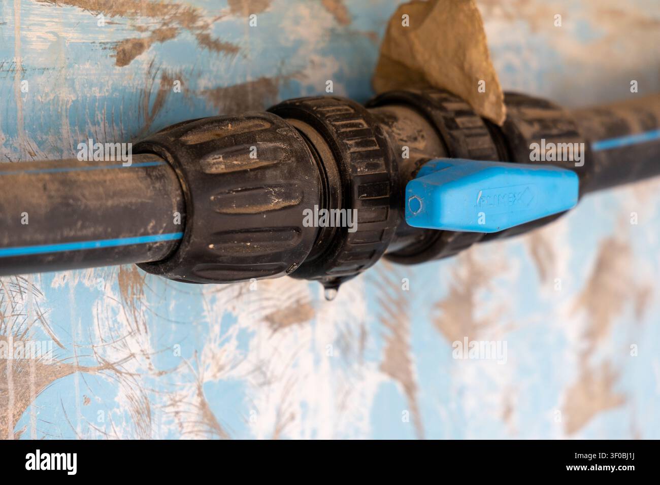 Une seule goutte d'eau est sur le point de tomber d'un raccord en plastique noir sale connecté à une vanne à bille bleue Banque D'Images