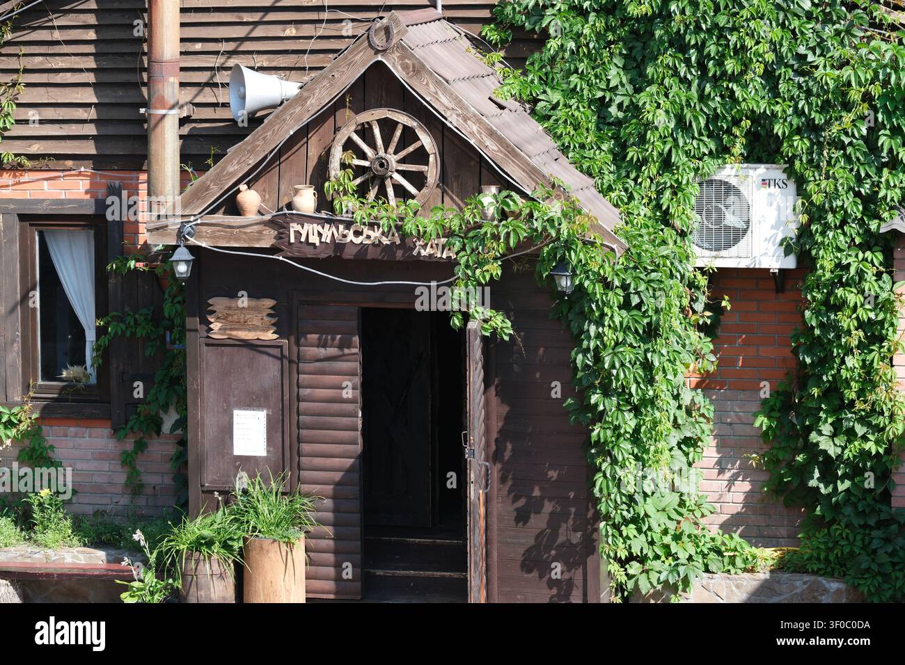 Kyiv, Ukraine - 7 juillet 2026 : Entrée d'un restaurant ukrainien traditionnel décorée d'architecture en bois rustique et de plantes grimpantes vertes dans le Banque D'Images