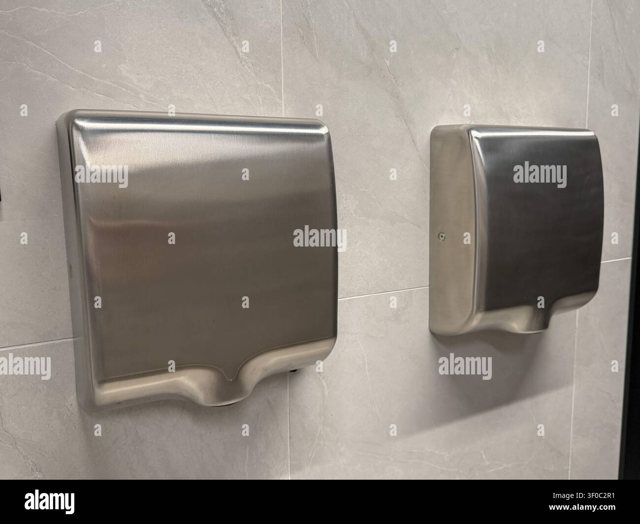 Séchoirs à mains en acier inoxydable montés sur un mur carrelé dans un intérieur de toilettes publiques modernes. Hygiène, assainissement, gestion des installations, technologie sans contact Banque D'Images