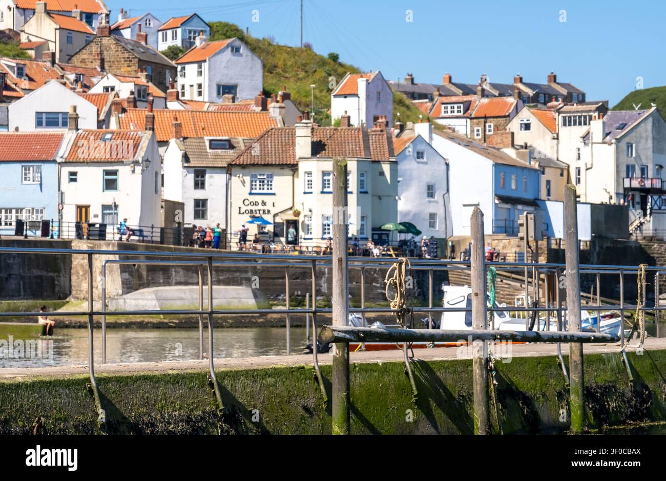Focus sélectif sur la jetée en béton et les poteaux d'amarrage en bois du port de Staithes, avec un arrière-plan légèrement flou mettant en valeur la texture et la côte Banque D'Images