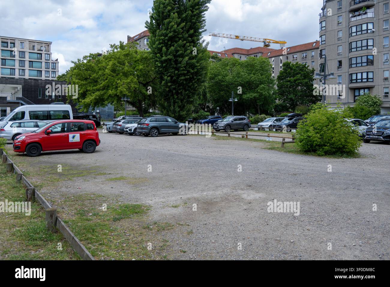 Berlin, Allemagne - 23 mai 25 : Zone de stationnement urbaine en gravier avec des voitures garées, des arbres et des immeubles d'habitation à Berlin, Allemagne. Banque D'Images