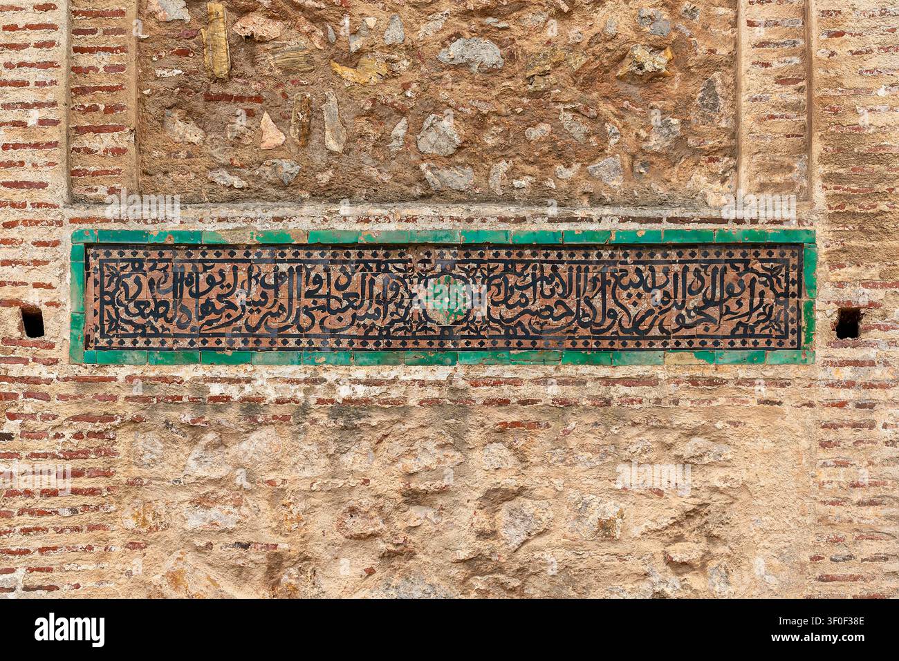 Un panneau rectangulaire de tuiles zellige vertes portant des inscriptions calligraphiques arabes est encastré dans un mur de briques de la kasbah, flanqué de plus petites de Banque D'Images