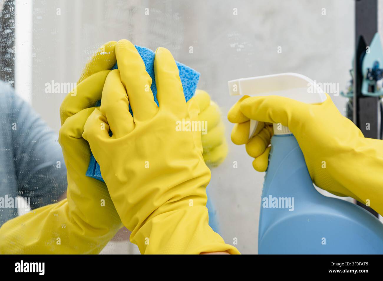 Nettoyage du miroir de la salle de bain avec une éponge bleue portant un gant en caoutchouc Banque D'Images