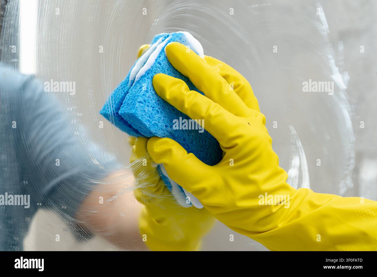 Nettoyage du miroir de la salle de bain avec une éponge bleue portant un gant en caoutchouc Banque D'Images