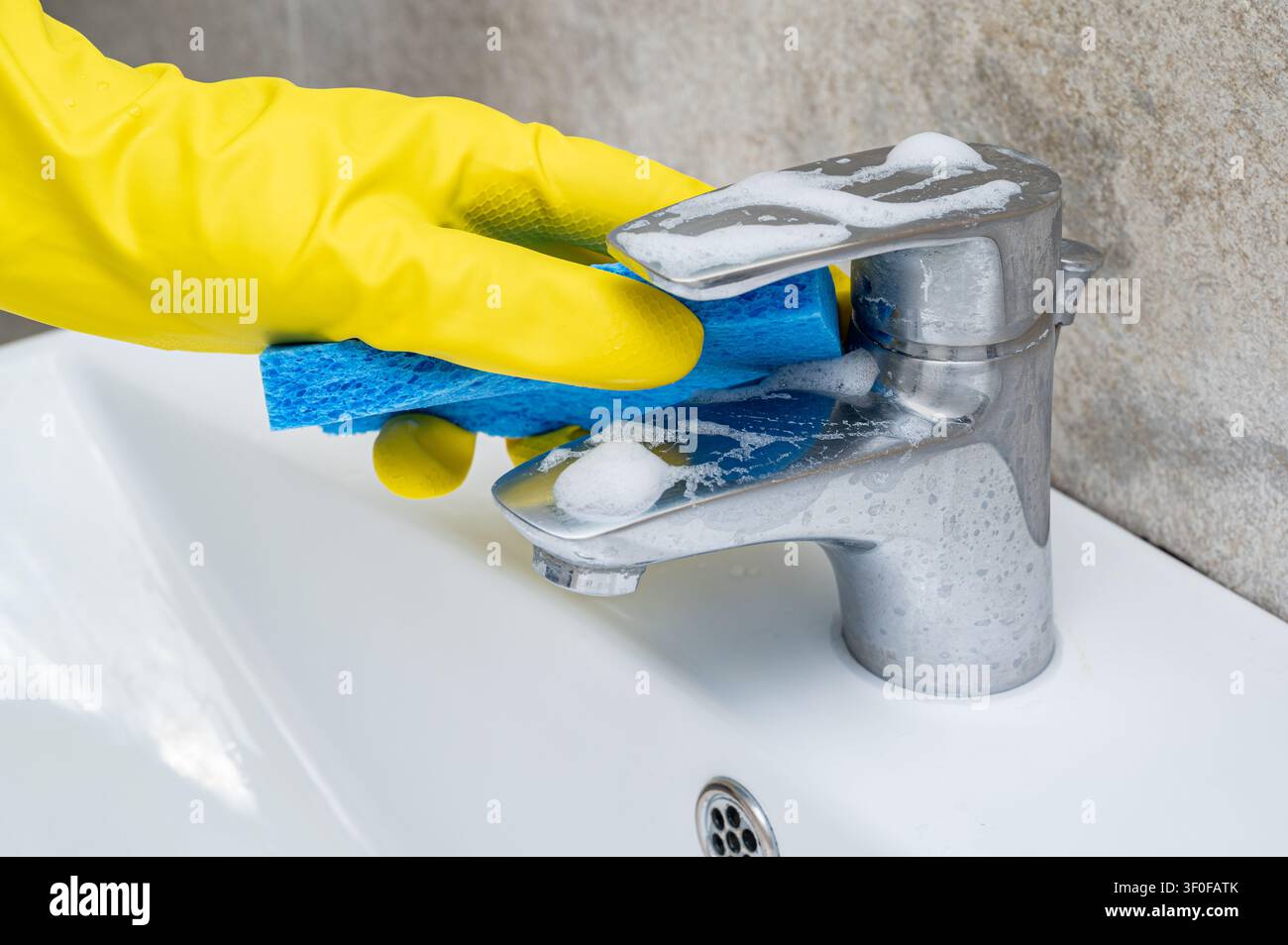 Nettoyage du robinet de la salle de bain avec une éponge bleue portant un gant en caoutchouc Banque D'Images