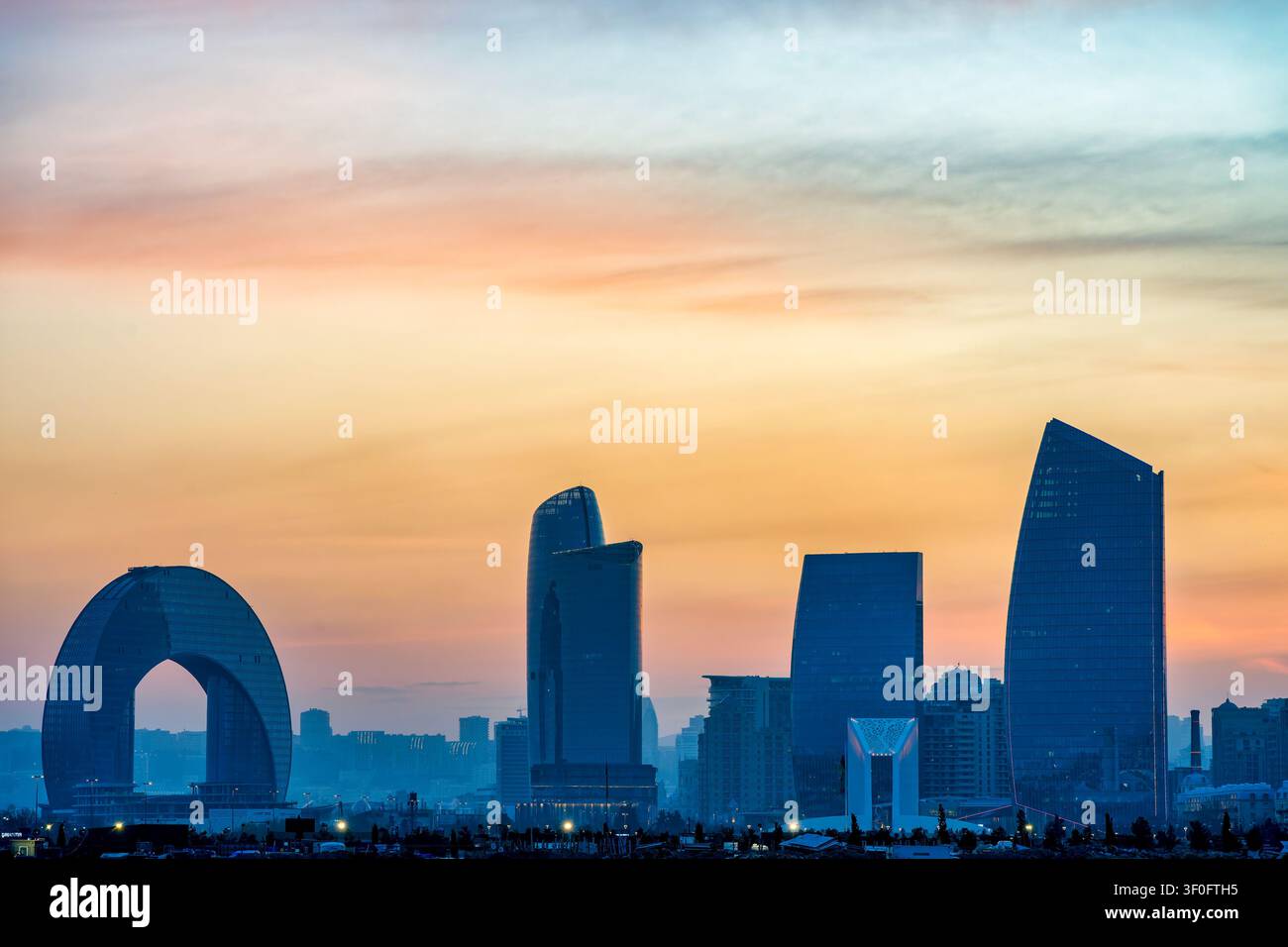 Silhouette de la skyline de Bakou au coucher du soleil mettant en scène l'hôtel Crescent, les Port Baku Towers et l'Arc de la Victoire contre un ciel orange doré. Bakou, Azerbaïdjan. Banque D'Images
