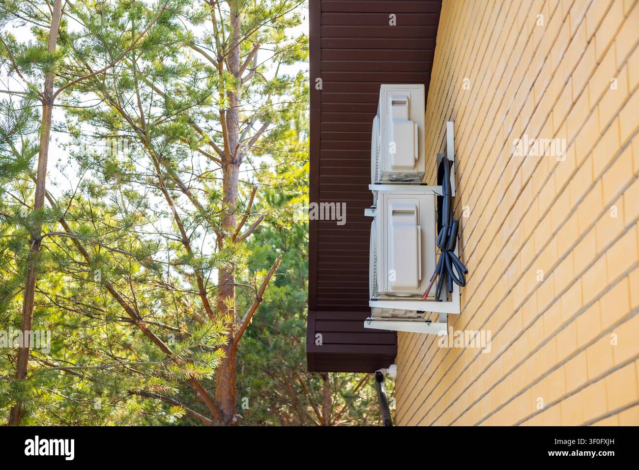 Deux unités de climatisation extérieures montées sur le mur d'une maison privée près de pins. Concept : refroidissement résidentiel Banque D'Images
