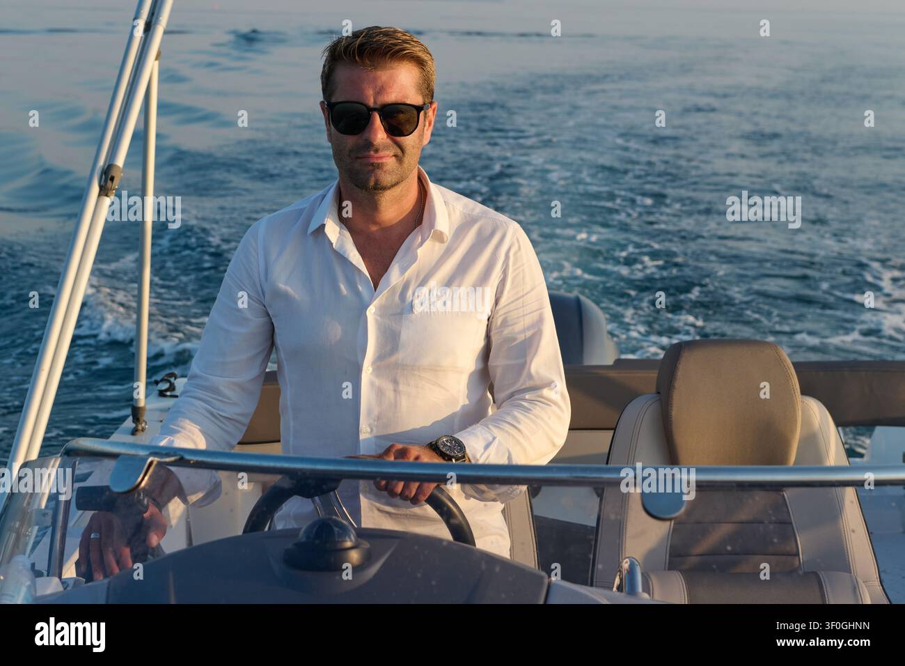 Homme confiant conduisant un bateau à moteur au coucher du soleil sur une mer calme pendant une croisière de loisir Banque D'Images