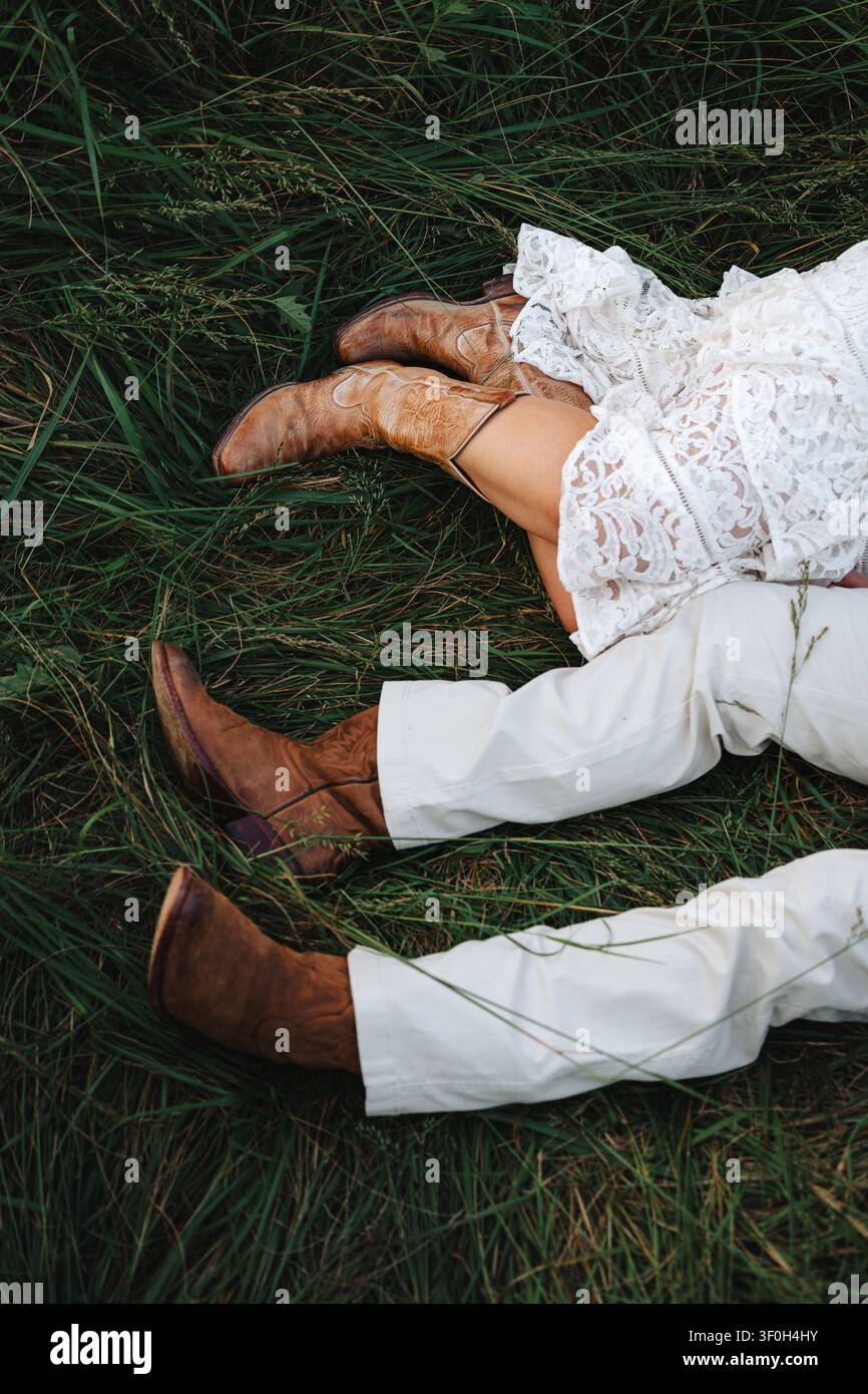 Couple en bottes de cowboy allongé ensemble dans une herbe haute et verte Banque D'Images