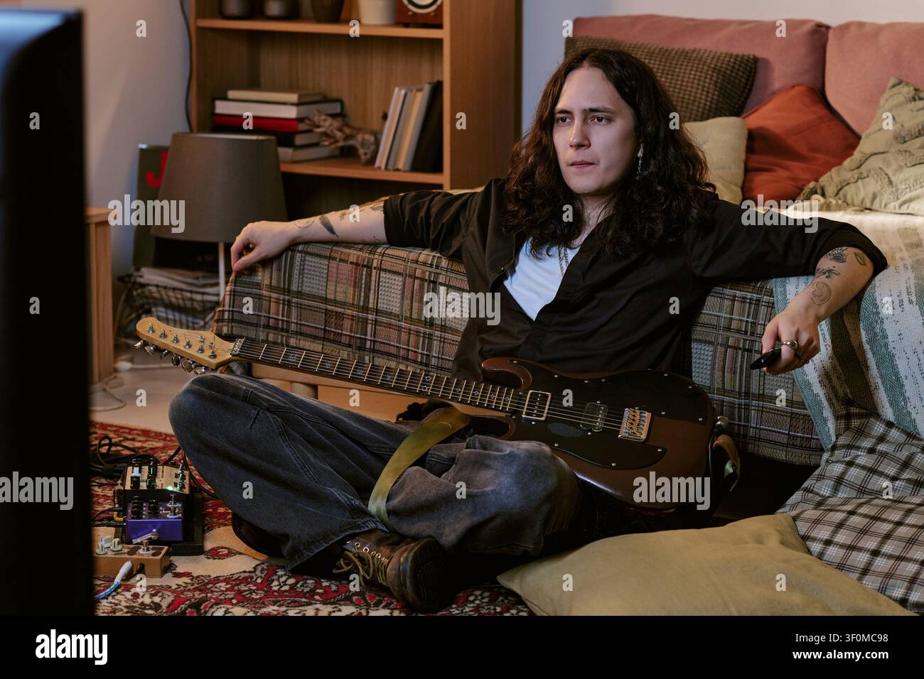 Musicien aux cheveux longs se détendant à la maison avec une guitare électrique Banque D'Images