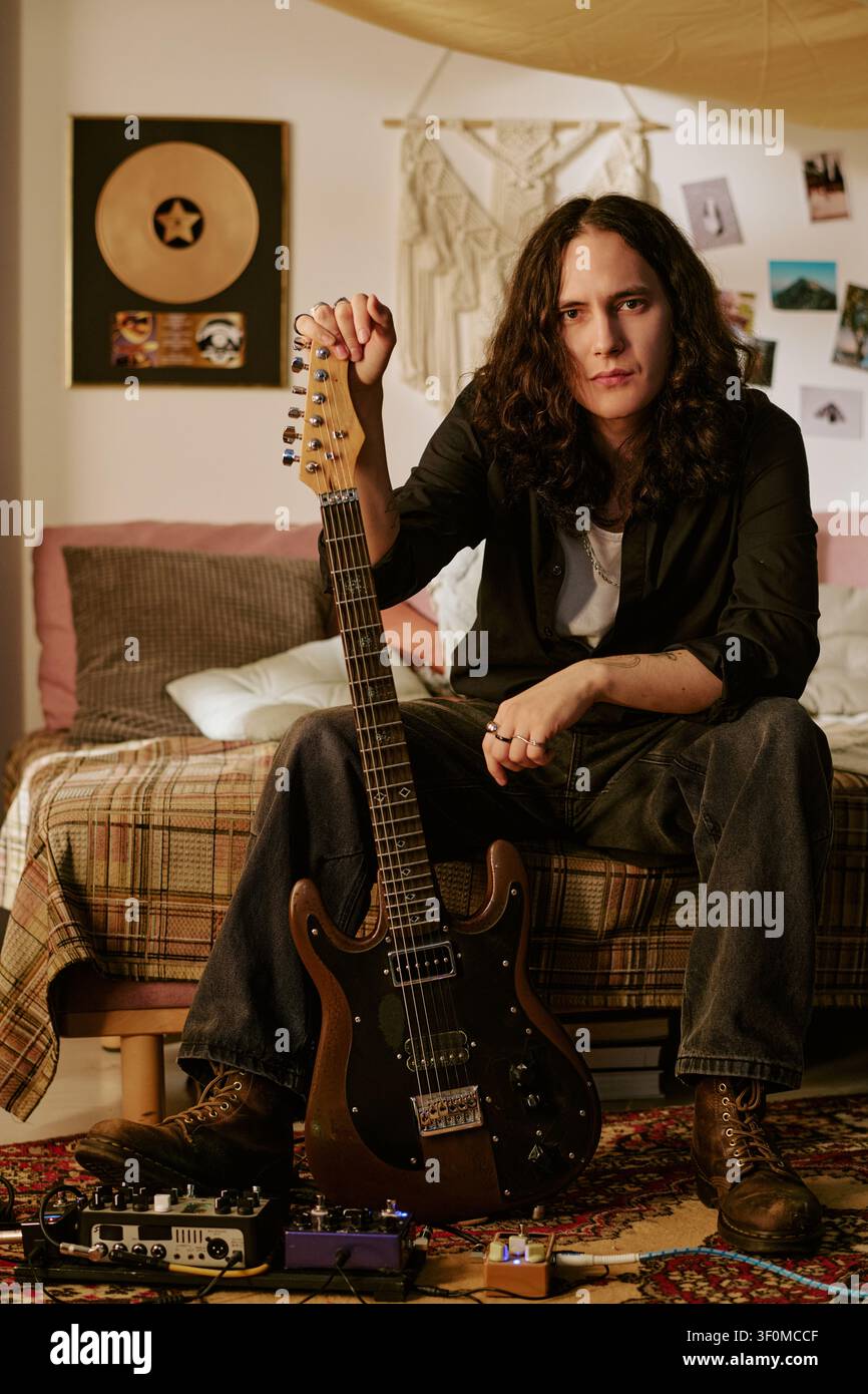 Portrait d'un homme aux cheveux longs tenant une guitare électrique dans un studio à domicile Banque D'Images