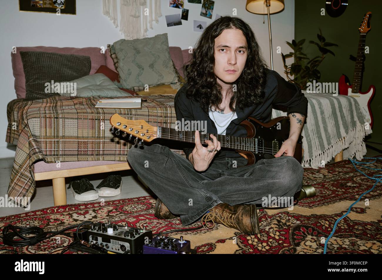 Portrait d'un homme aux cheveux longs jouant de la guitare électrique dans son studio à domicile Banque D'Images