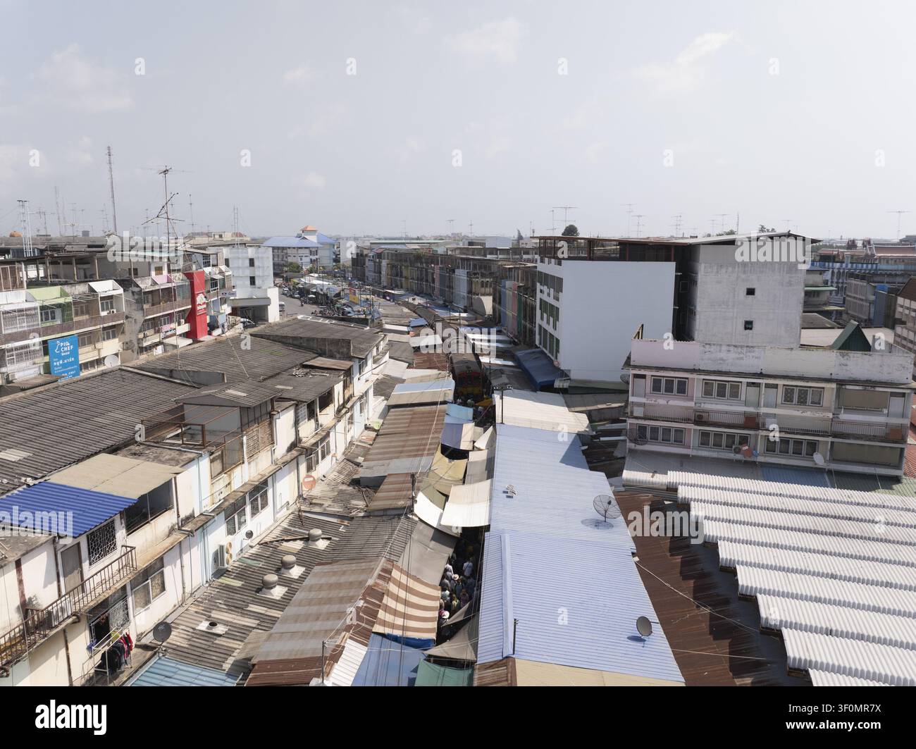 Vue aérienne du marché ferroviaire de Maeklong avec un train traversant la zone urbaine dense, mettant en vedette des auvents colorés et des toits à Mae Kl Banque D'Images