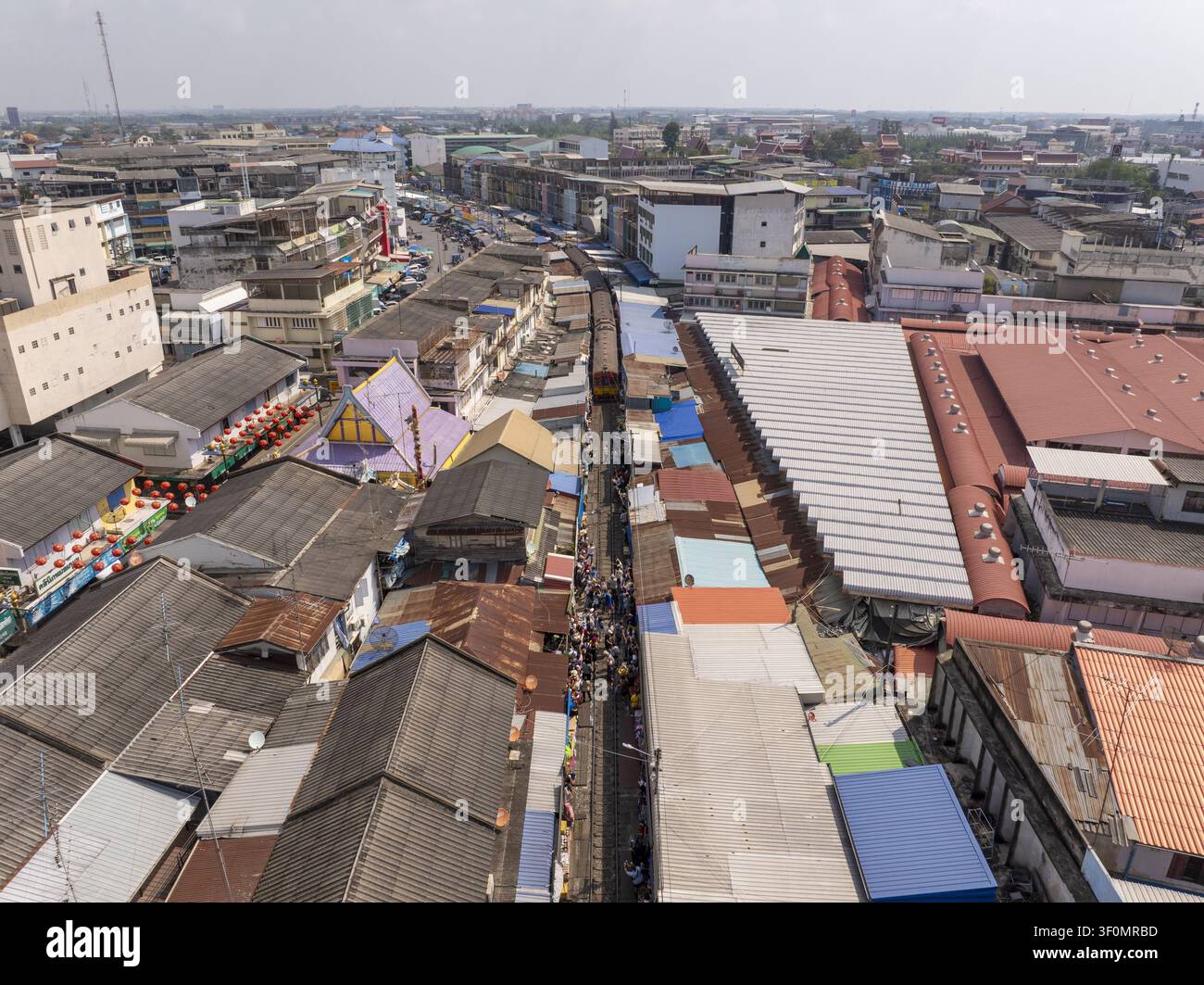 Vue aérienne du marché ferroviaire de Maeklong avec un train approchant sur les voies bordées de rangées denses d'étals de marché colorés et de toits à Mae Klong, S Banque D'Images