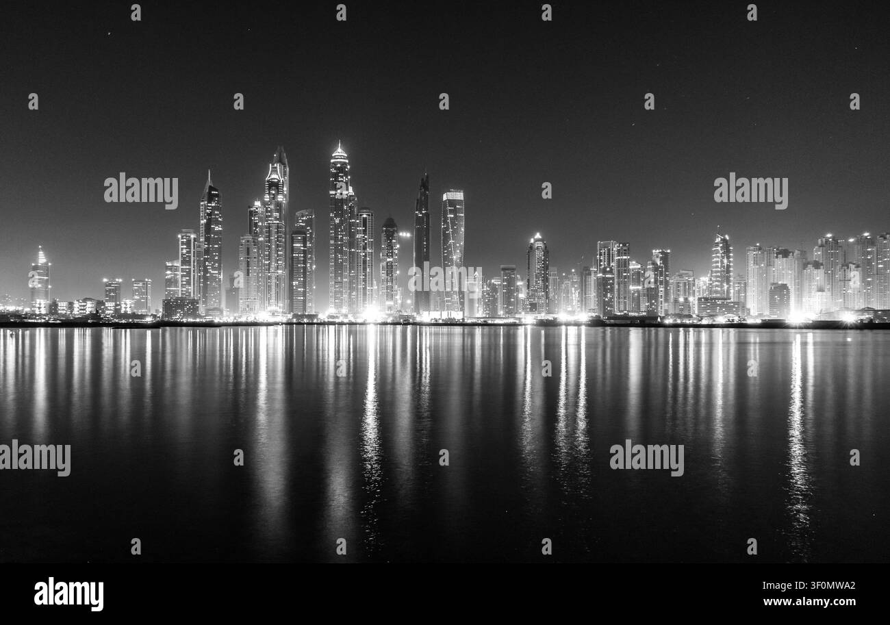 Une vue panoramique en noir et blanc à longue exposition capture l'horizon emblématique de Dubai Marina tel qu'il est vu à travers des eaux calmes du front de mer. Banque D'Images