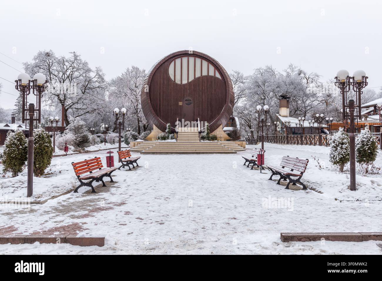 Une grande structure architecturale en forme de tonneau à vin en bois se dresse au centre d'un parc enneigé. Banque D'Images