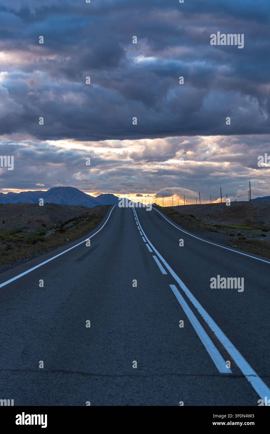 Une autoroute rectiligne à deux voies en asphalte traverse la steppe aride des hautes terres de la république de l'Altaï dans le sud de la Sibérie, en Russie. Banque D'Images