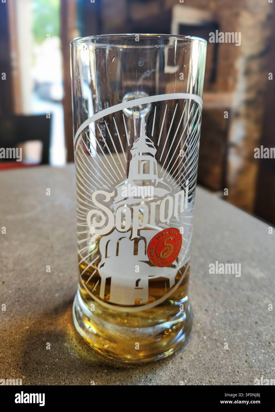 Un verre de bière de la marque Soproni presque vide sur une table en béton dans un cadre de restaurant, avec une faible profondeur de champ Banque D'Images