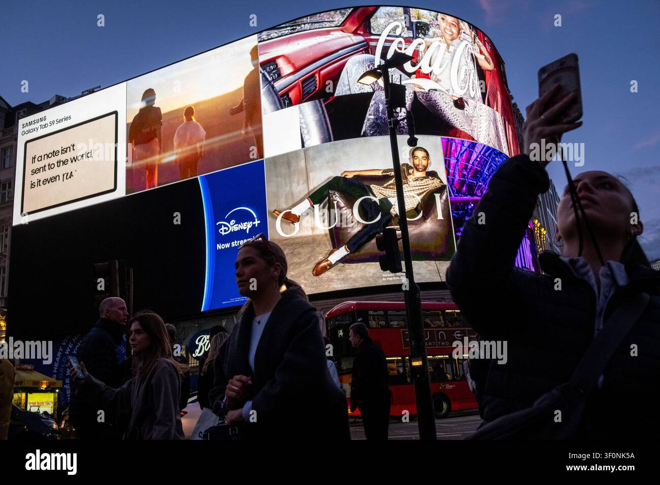 Les piétons se tiennent sous des écrans LED incurvés illuminés montrant une publicité pour la Samsung Galaxy Tab S9, un logo Disney Plus Now Streaming, Coca Cola et Banque D'Images
