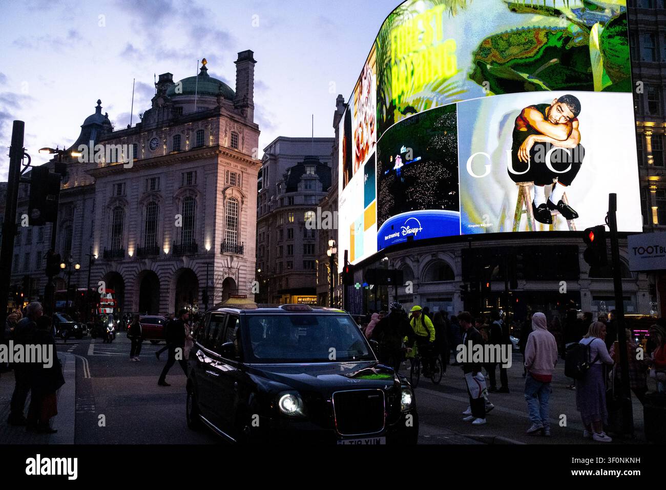 Un taxi noir passe sous des panneaux publicitaires numériques illuminés affichant Gucci et Disney ainsi que des publicités à Piccadilly Circus, Londres, Angleterre, Royaume-Uni Banque D'Images