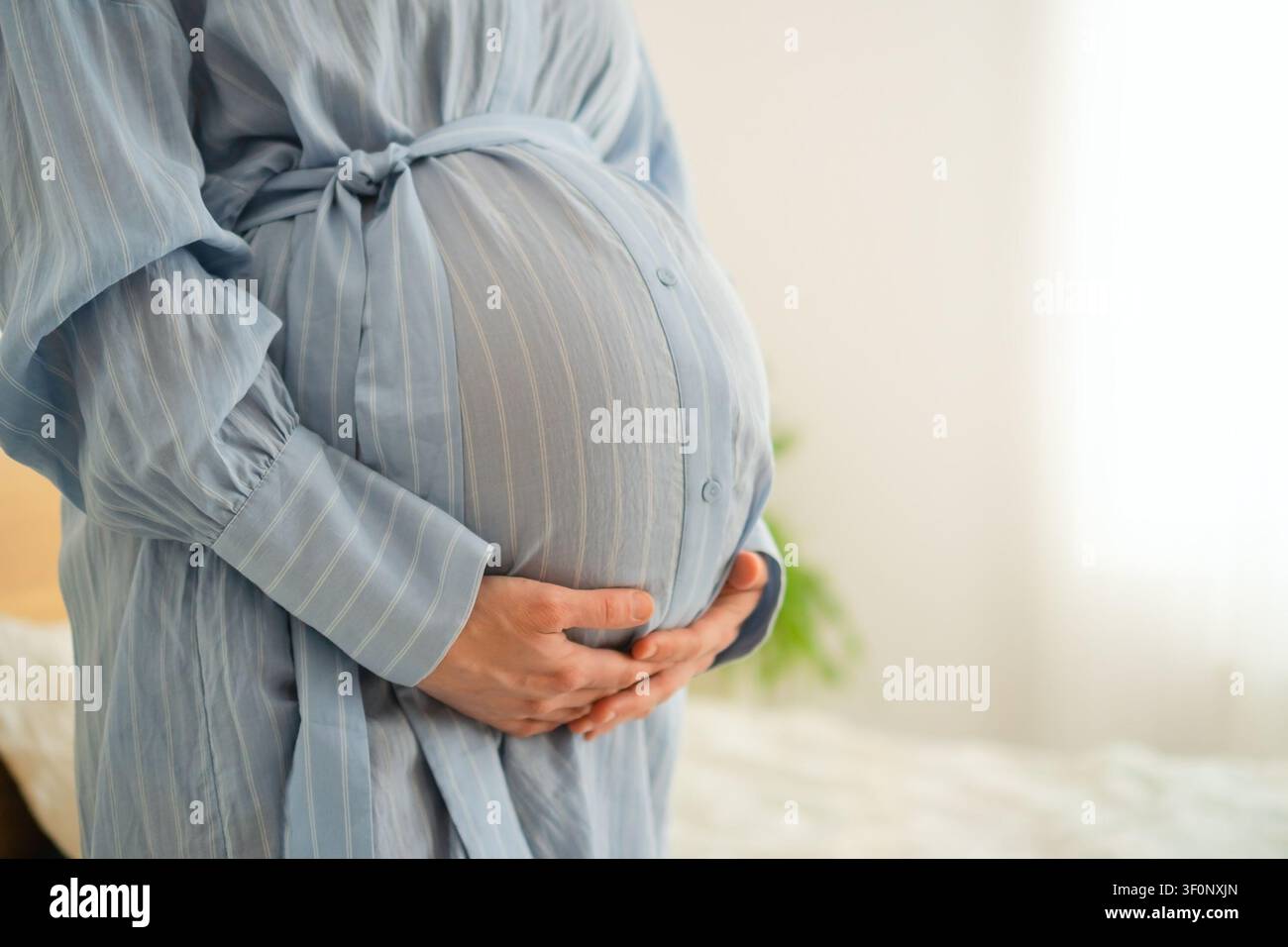 Femme enceinte de dos avec les mains sur le ventre en robe bleue sur fond blanc. Mère enceinte dans une pose détendue et confiante en studio. Future maman montrant une maternité heureuse dans une élégante tenue de maternité Banque D'Images