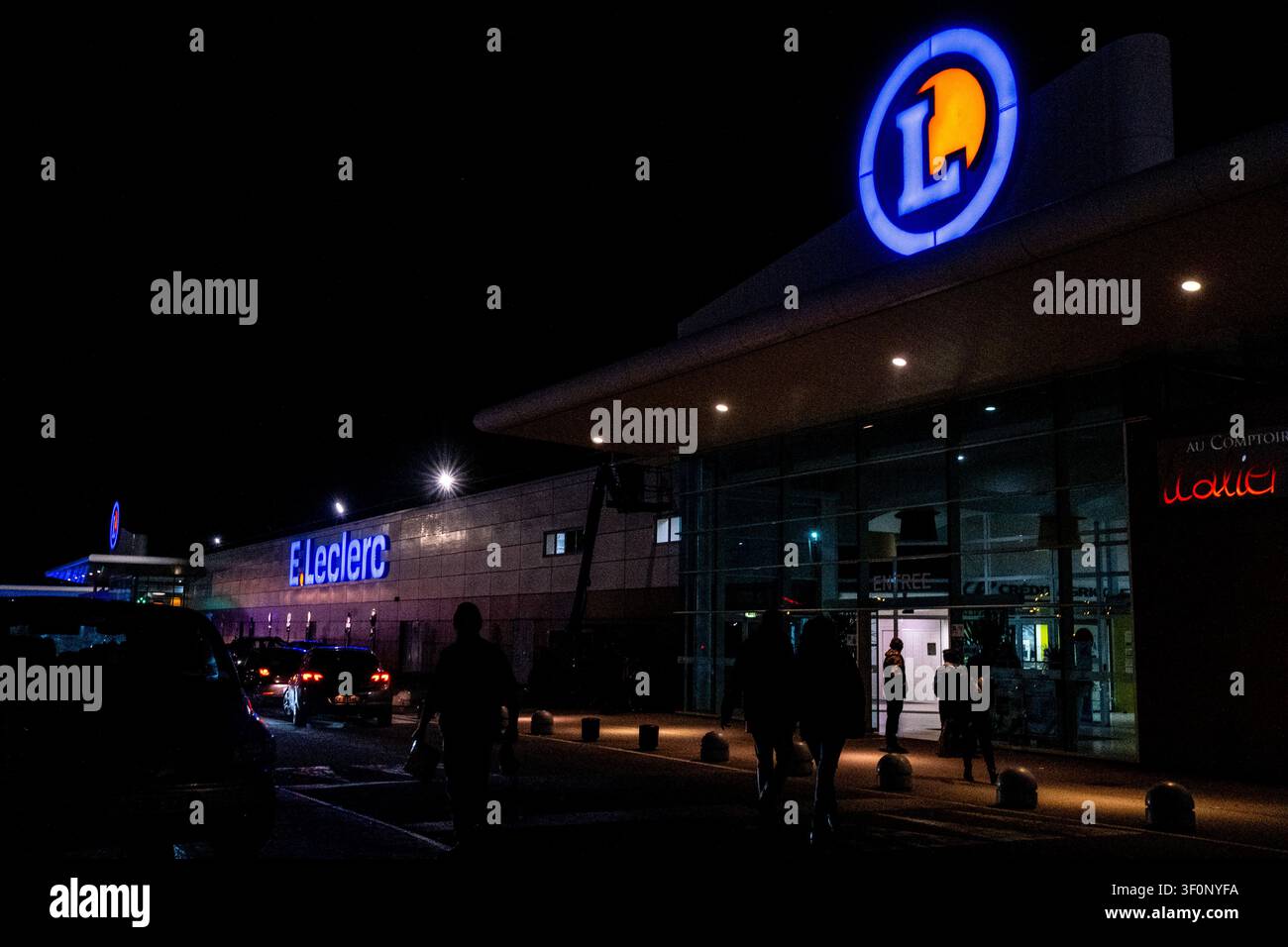 Vue extérieure nocturne d'un supermarché et centre commercial E.Leclerc avec enseignes éclairées, clients et voitures dans la région de Dinan, Bretagne, France o Banque D'Images