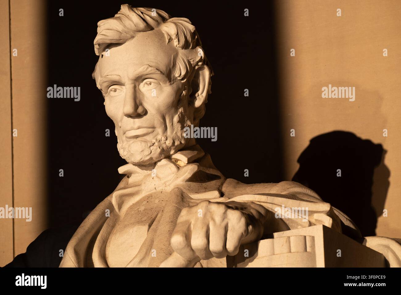 Détail de l'épaule de la statue de Lincoln à Washington DC | WASHINGTON D.C., États-Unis — Le lever de soleil à l'équinoxe projette une longue ombre à côté de l'épaule et du bras tendu de la statue de Lincoln en marbre à l'intérieur du Lincoln Memorial. Les 28 blocs de marbre du sculpteur Daniel Chester French ont été taillés séparément dans le Bronx et jamais ajustés avant d'arriver à Washington, mais le National Park Service note que les coutures sont arrivées presque invisibles. Banque D'Images